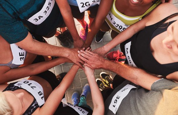 High angle portrait of a sports team standing in a circle with their hands stacked. Team of runners with hands together after competition.